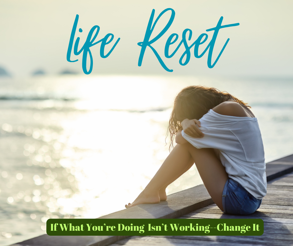 Woman sitting on a dock with her head covered and resting on her knees, appearing emotional as she thinks about how to reset and rebuild your life
