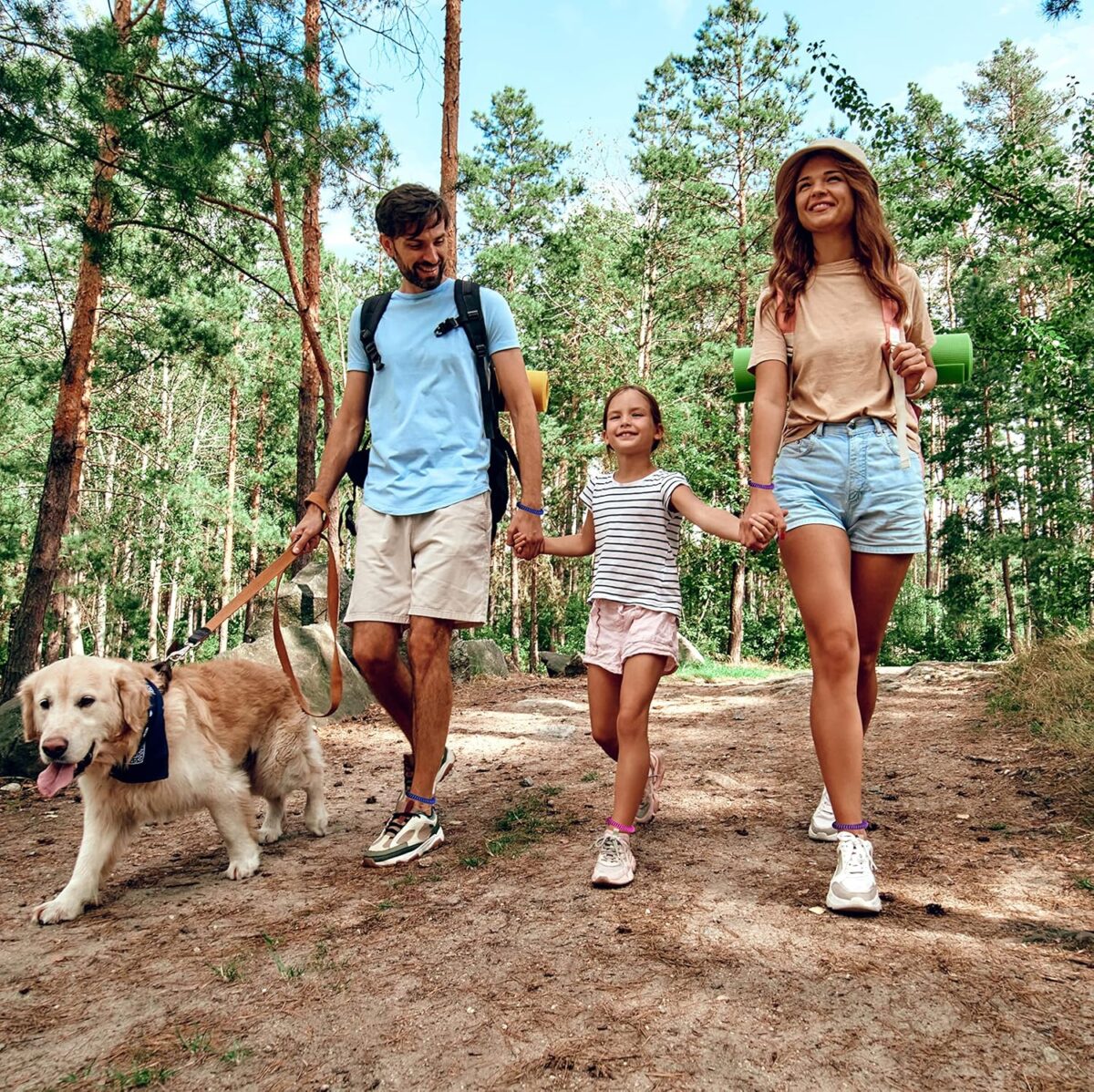 A family of three walking their dog on a peaceful nature trail while wearing  mosquito-repellent bracelets for a calm, enjoyable evening outdoors.